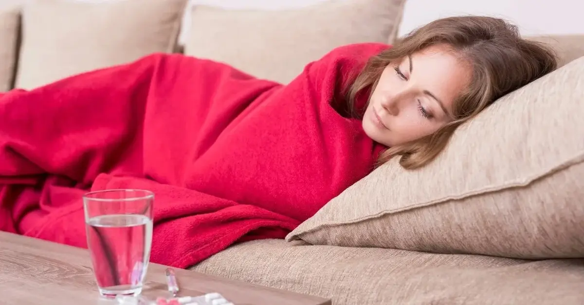 Kobieta leżąca na kanapie pod czerwoną kołdrą