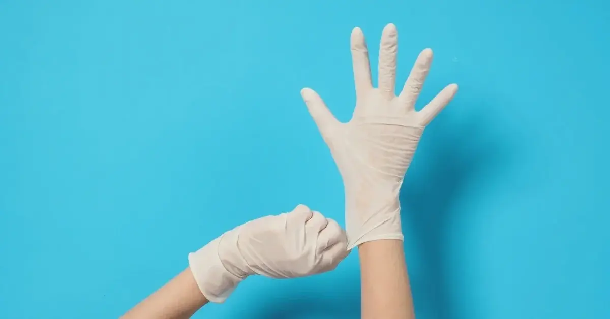 Ręce osoby z założonymi bialymi rękawiczkami lateksowymi 