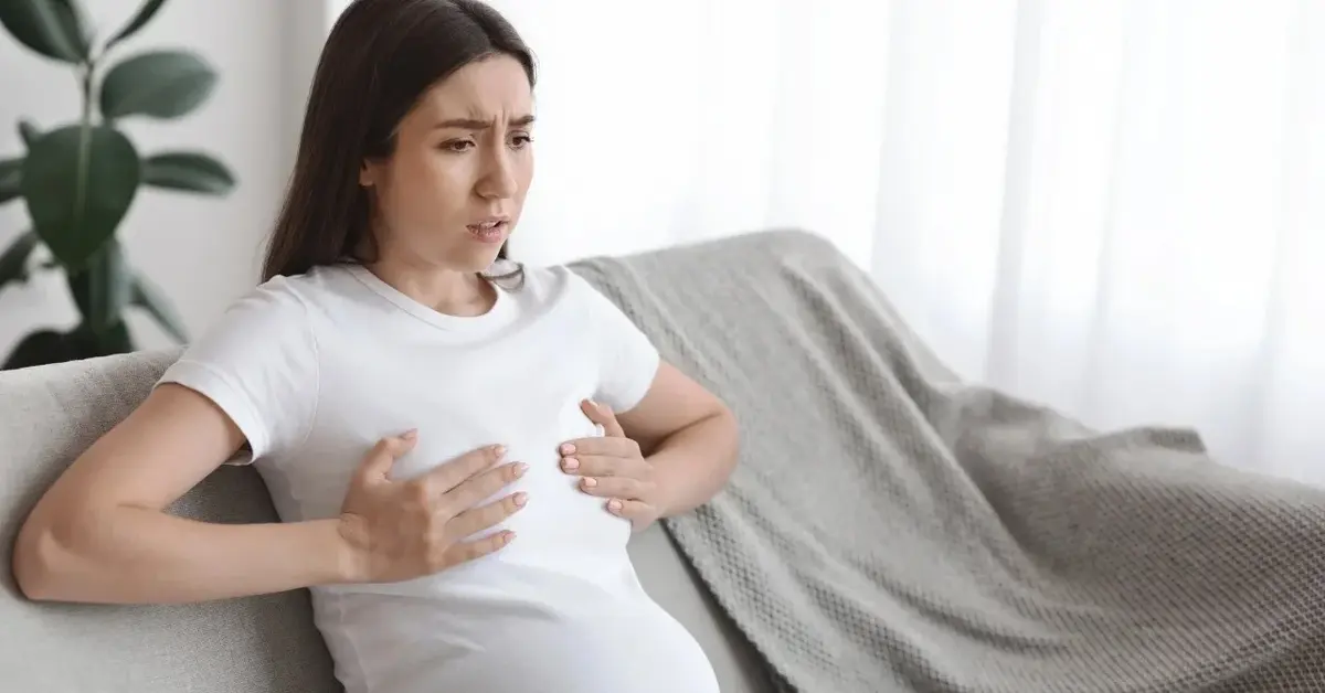 Kobieta siedząca na kanapie i trzymająca się za piersi