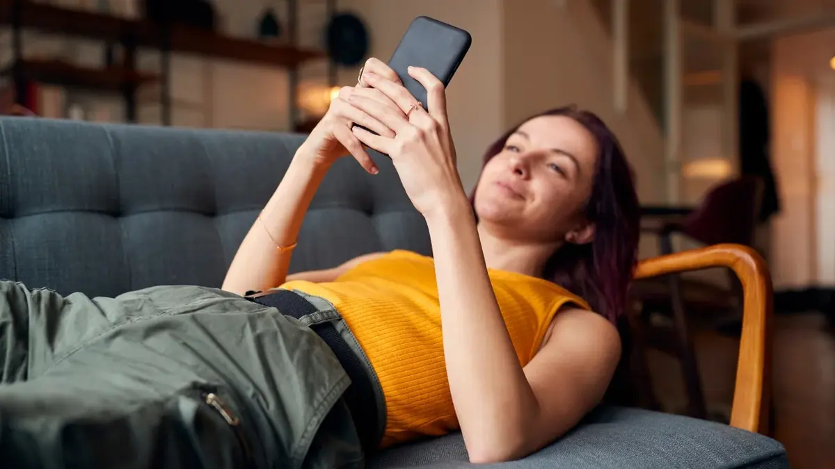 Kobieta leżąca na kanapie z telefonem w rękach 