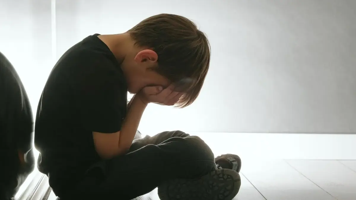 Chłopiec siedzący na podłodze z twarzą schowaną w dłoniach 