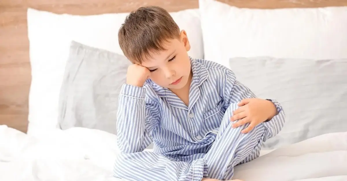 Chłopiec siedzący na łóżku opierający głowę na ręce