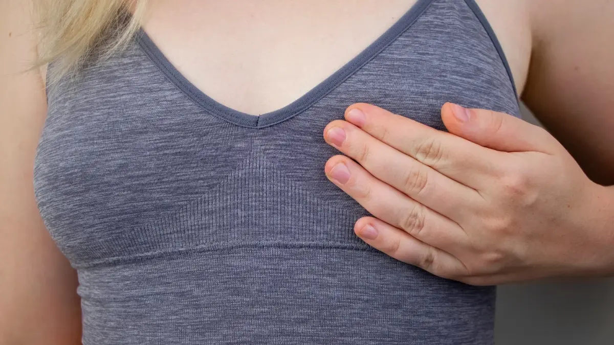 Kobieta w szarej koszulce trzymająca rękę na piersi 