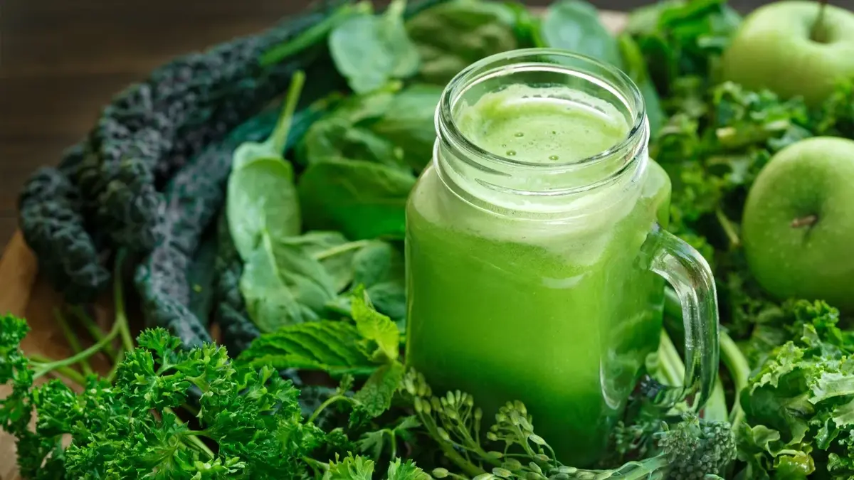 Zielony sok w szklance, obok warzywa i owoce 