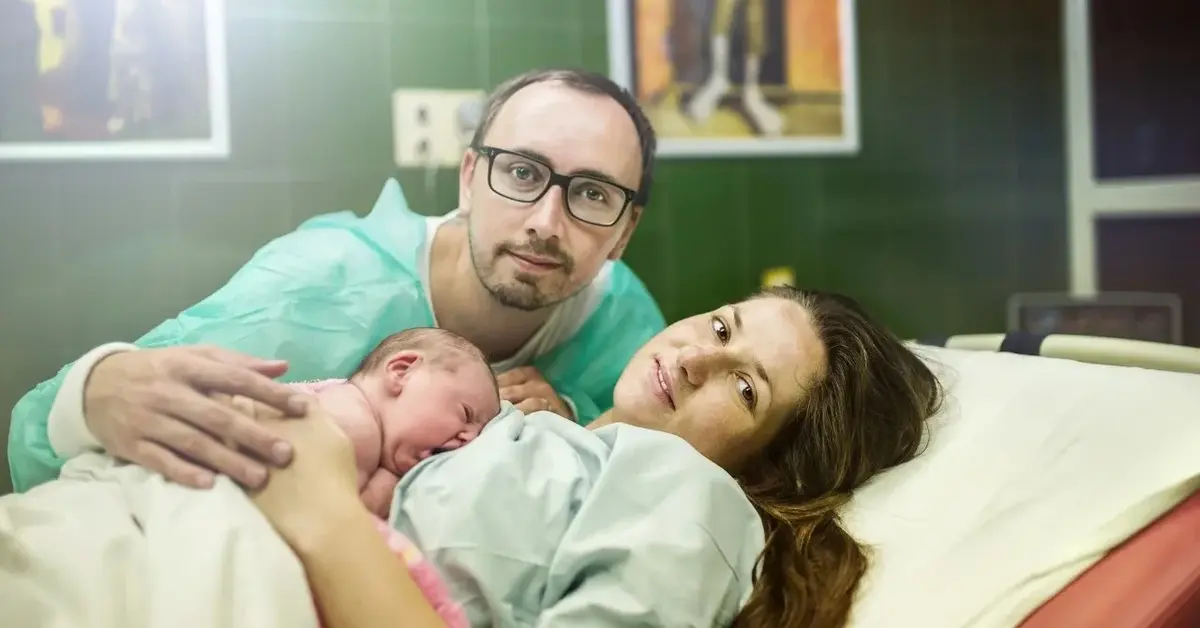 kobieta trzymająca noworodka na piersi i meżczyzna przytulający ich