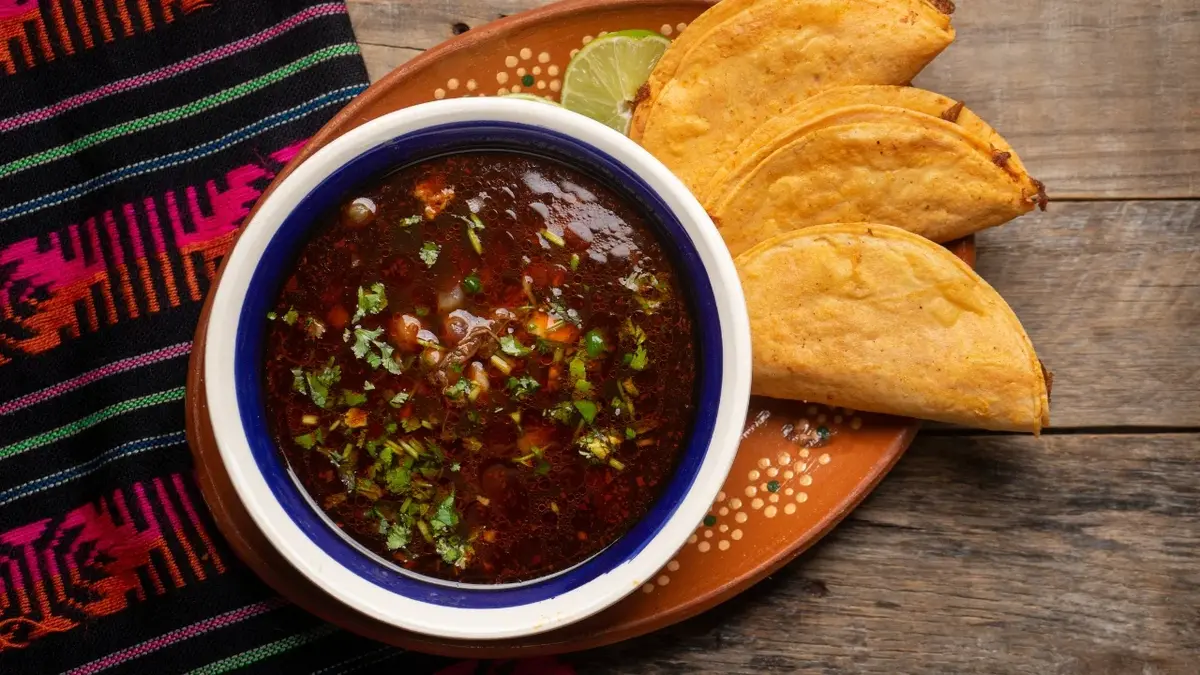 Zupa meksykańska w miseczce stojącej na talerzyku. Obok meksykańskie tortille