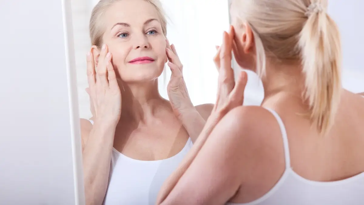 Kobieta smarująca twarz kremem z kolagenem przed lustrem
