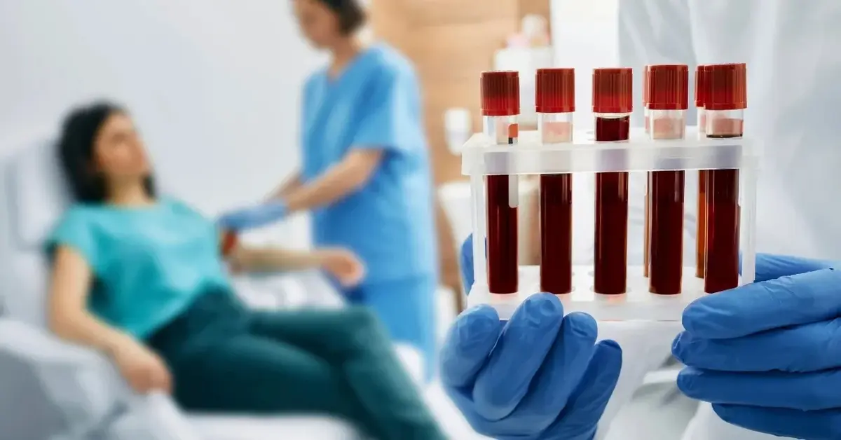 Próbki z pobraną krwią, w tle kobieta podczas pobierania krwi przez pielęgniarkę 