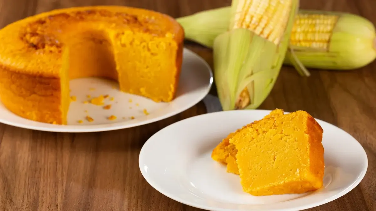 Porcja ciasta kukurydzianego na talerzyku, w tle reszta ciasta i kolby kukurydzy