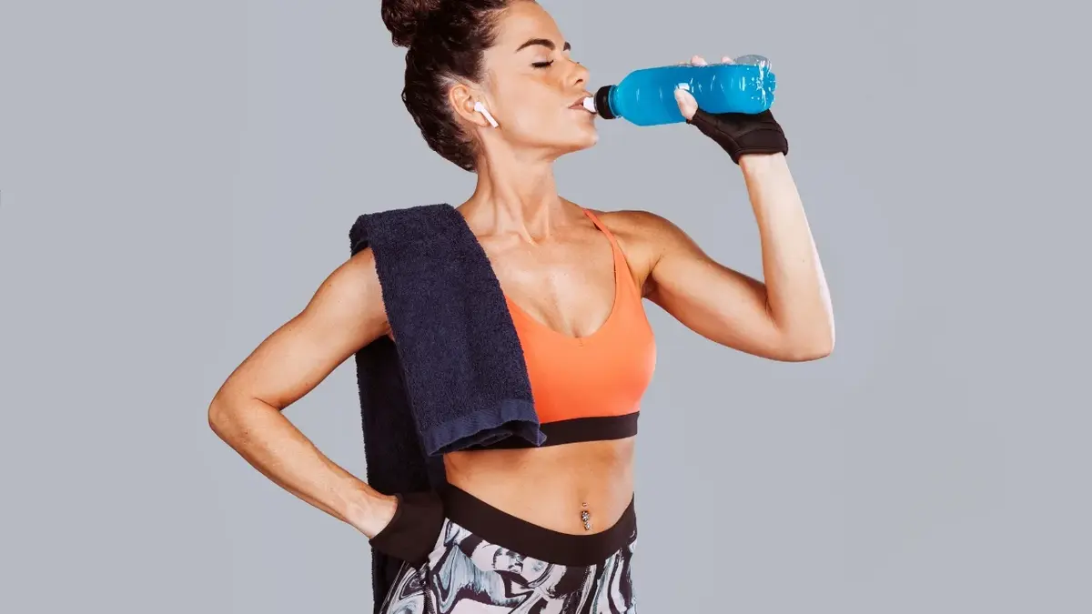 Kobieta w stroju sportowym pijąca izotonik 