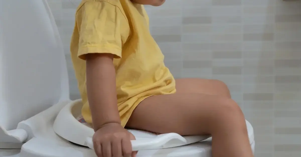 Dziecko w żółtej koszulce siedzące na toalecie