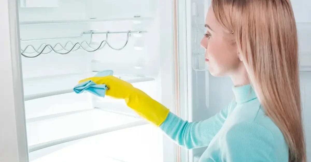Kobieta myjąca lodówke w żółtych rękawiczkach 