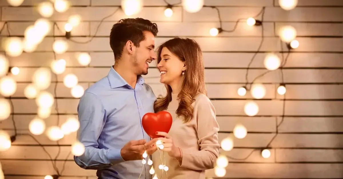 Kobieta i mężczyzna przytuleni na tle podświetlonej ściany trzymający w ręce czerwone serce