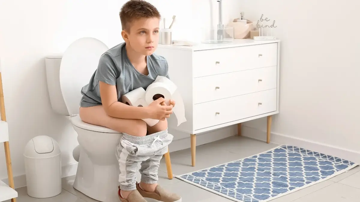 Chłopiec siedzący na toalecie trzymający papier toaletowy w dłoniach 
