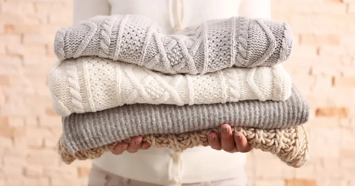 Wyprane wełniane swetry złożone w kostkę i trzymane w rękach 
