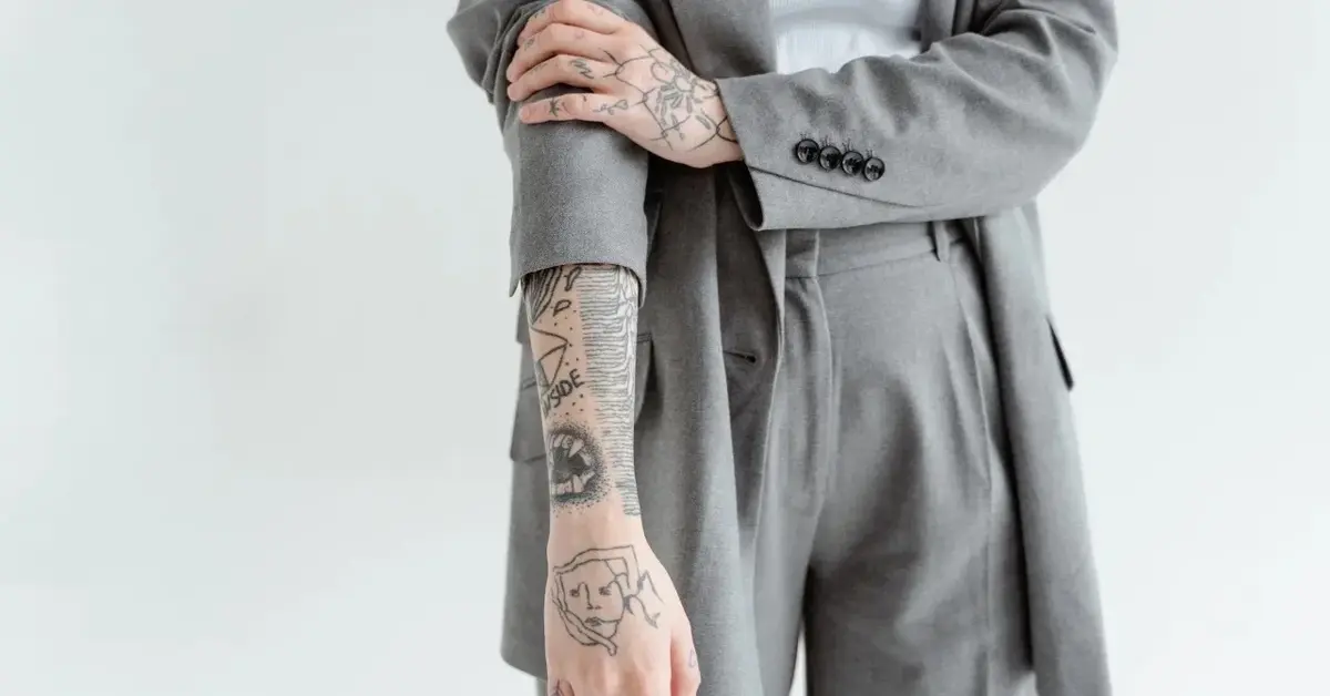 Kobieta w garniturze odsłaniająca rękaw i pokazująca tatuaże na rękach 