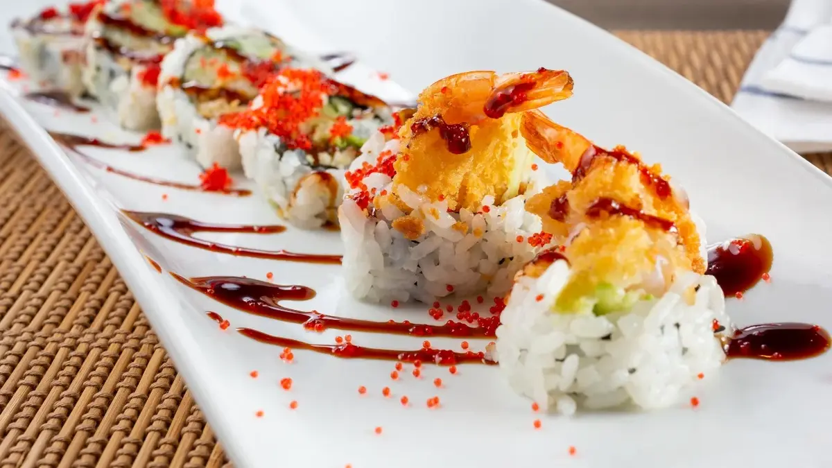Krewetki w tempurze ułożone na rolkach sushi na długim białym półmisku