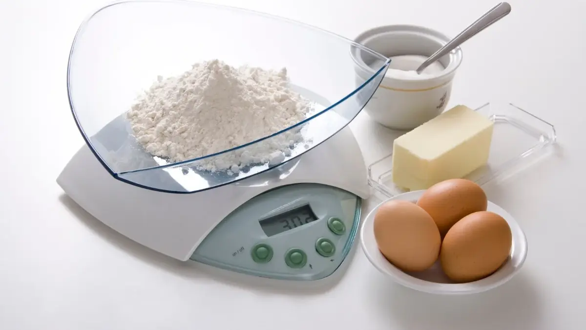 Mąka na wadze kuchennej, obok masło, jajka i cukier