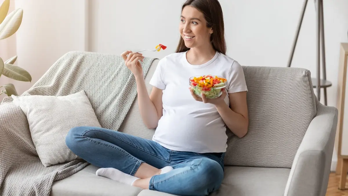 Kobieta w ciąży na kanapie jedząca sałatkę