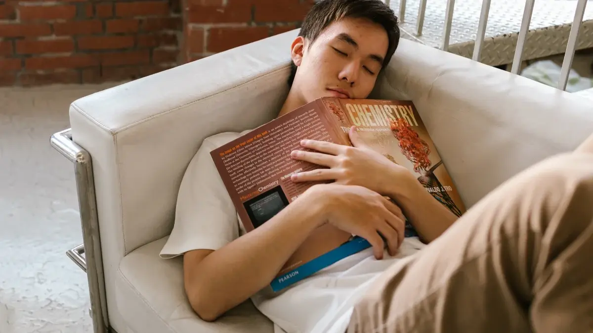 Nastolatek śpiący na kanapie z książką w ręku 