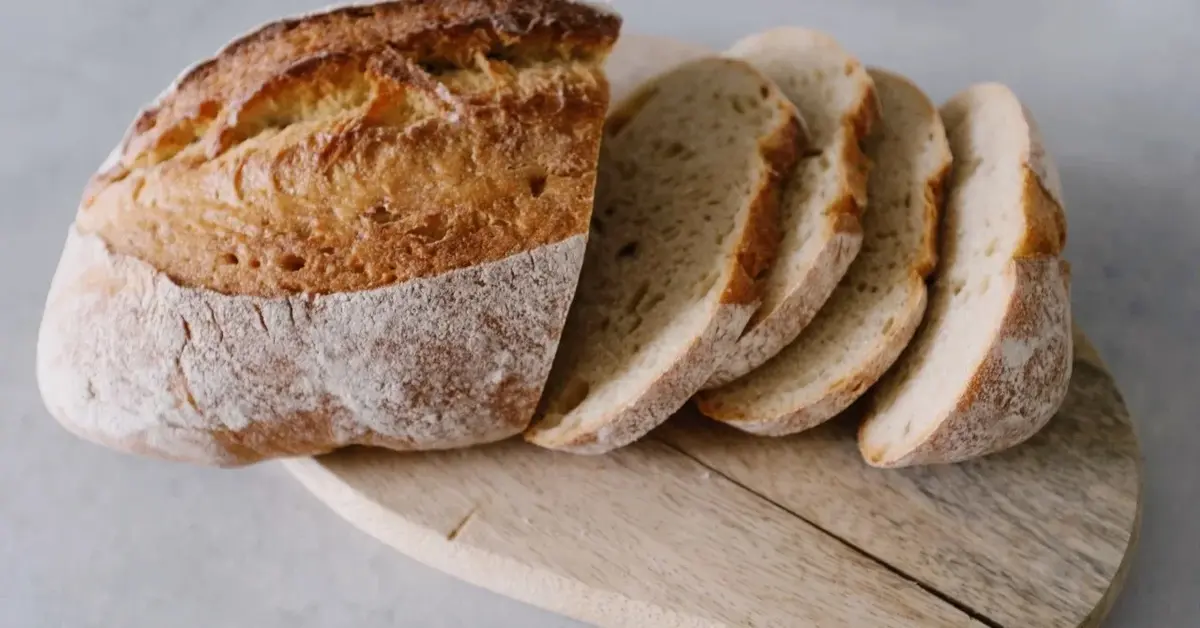 Bochenek chleba  z kilkoma ukrojonymi kromkami na drewnianej desce i białym tle 