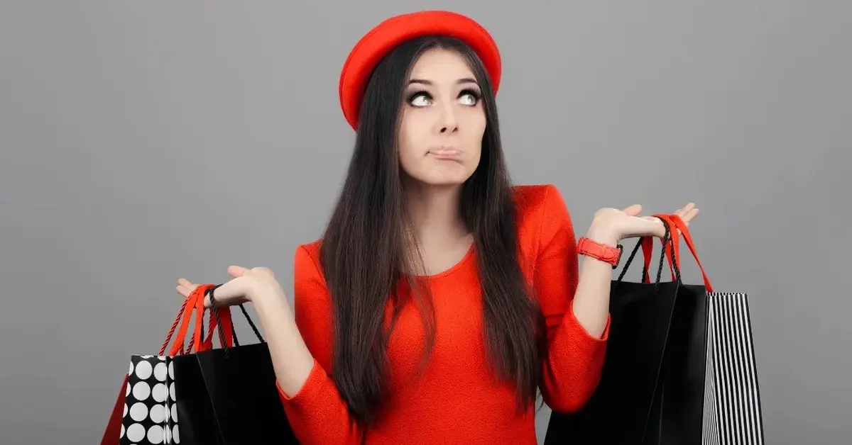 Kobieta w czerwonej sukience i czerwonym berecie trzymająca w rękach torby z zakupami 