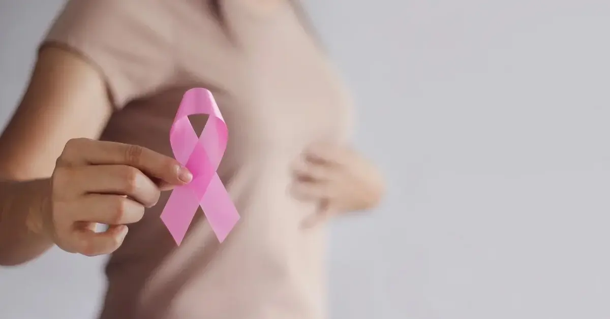 kobieta trzymająca w ręce różową wstążkę symbol raka piersi 