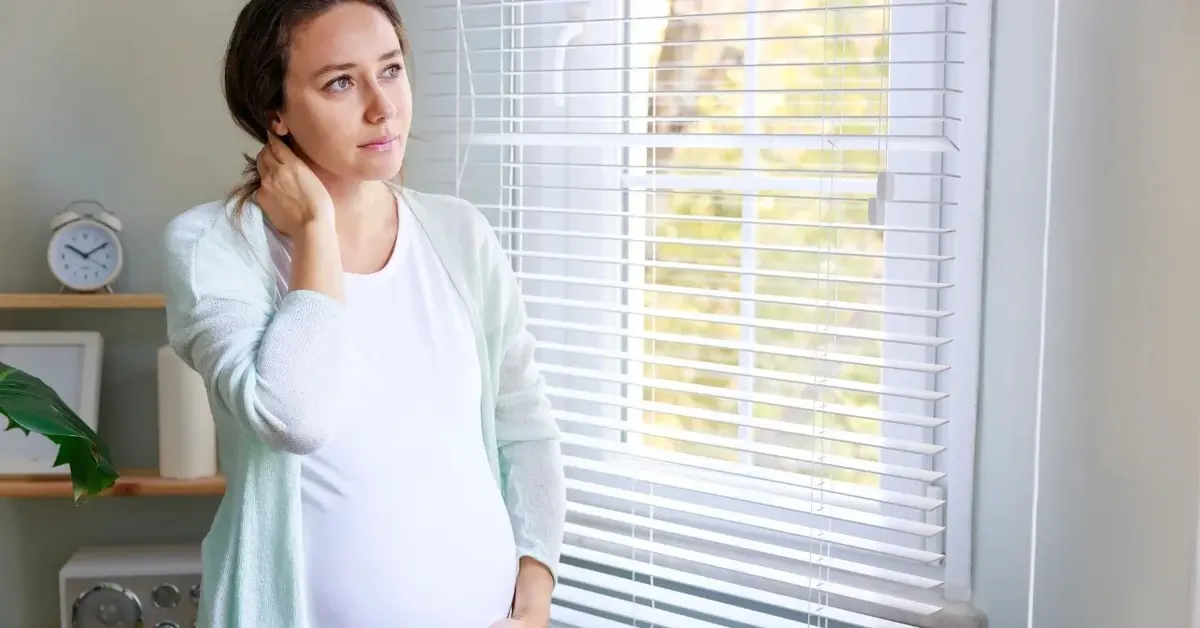 Kobieta w ciąży stojąca obok okna