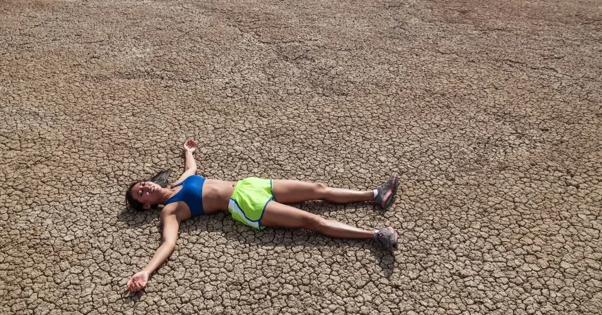 Kobieta w krótkich spodenkach leżąca na spękanej od gorąca ziemi
