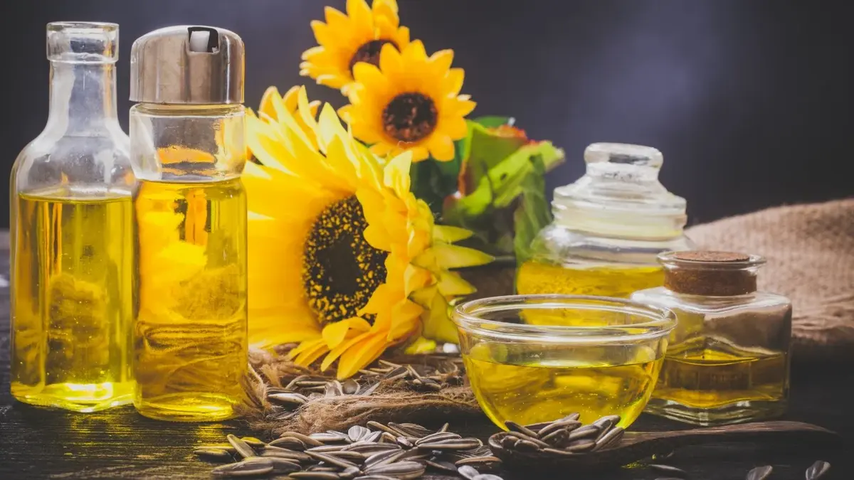Olej słonecznikowy w buteleczkach i miseczce, obok kwiaty słonecznika 