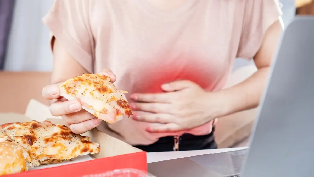 Kobieta trzymająca sie za brzuch ręką, drugą siegająca po kawałek pizzy
