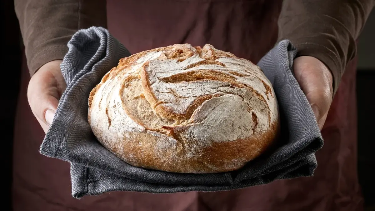Bochenek chleba trzymany na ściereczce