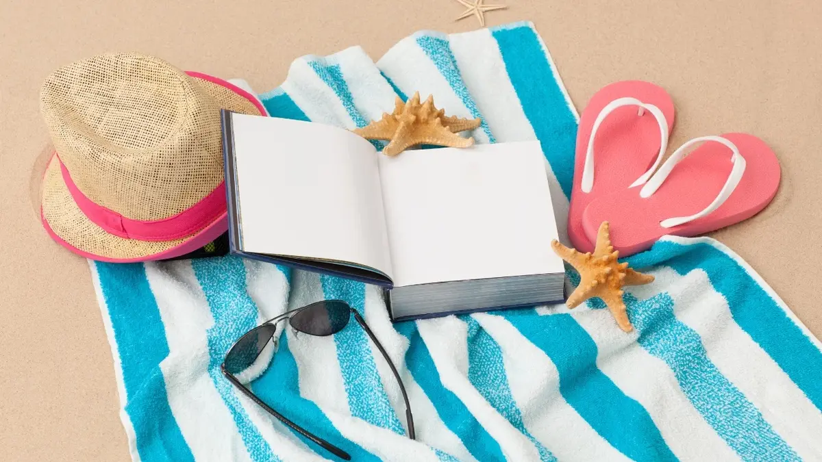 Książka, okulary przeciwsłoneczne i japonki na ręczniku plażowym 