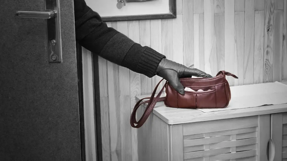Ręka w czarnej rękawiczce sięgająca po torebkę leżącą na szafce koło drzwi 