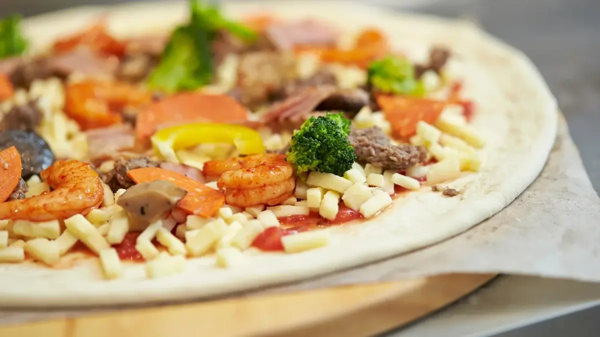 Nieupieczona pizza z równymi dodatkami: serem, krewetkami, brokułami na drewnianej desce