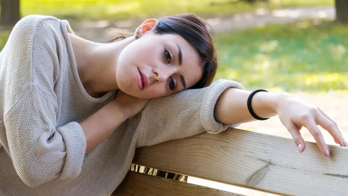 Dziewczyna w parku siedząca na ławce oparta o rękę 