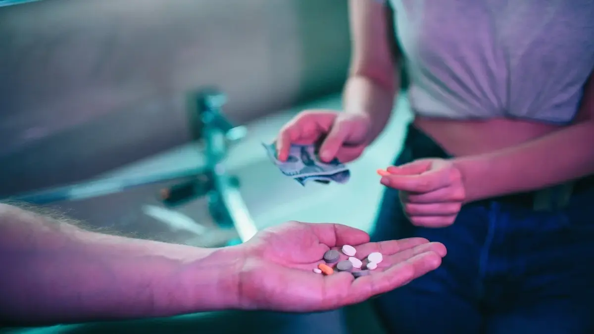 Reka osoby z tabletkami w dłoni i druga osoba sięgające po nie
