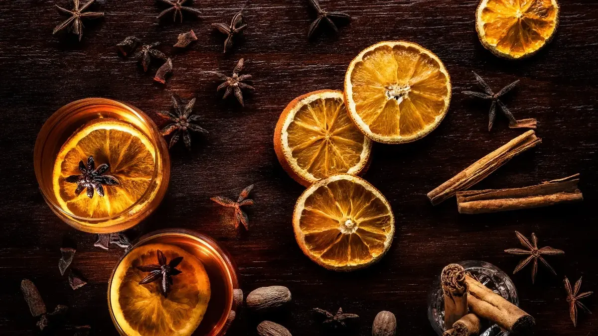Suszone pomarańcze na stole, obok herbata z plasterkami suszonej pomarańczy, laski cynamonu i gwiazdki anyżu 