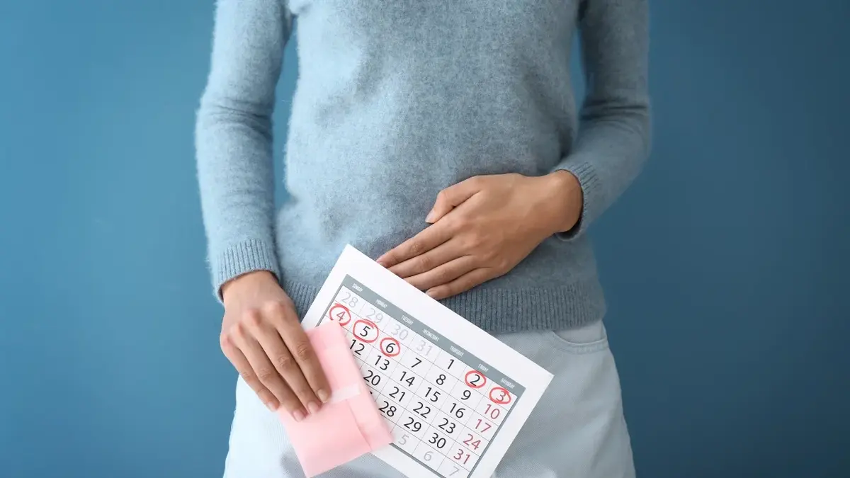 Kobieta w niebieskim swetrze na tle niebieskiej ściany trzymająca w ręce kartkę z kalendarza 