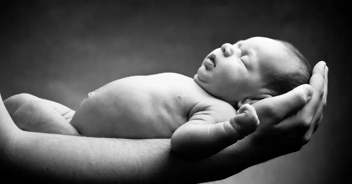 Czarno-białe zdjecie noworodka trzymane na rękach 