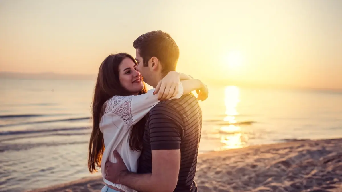 Przytulająca się para na plaży an tle zachodzącego słońca