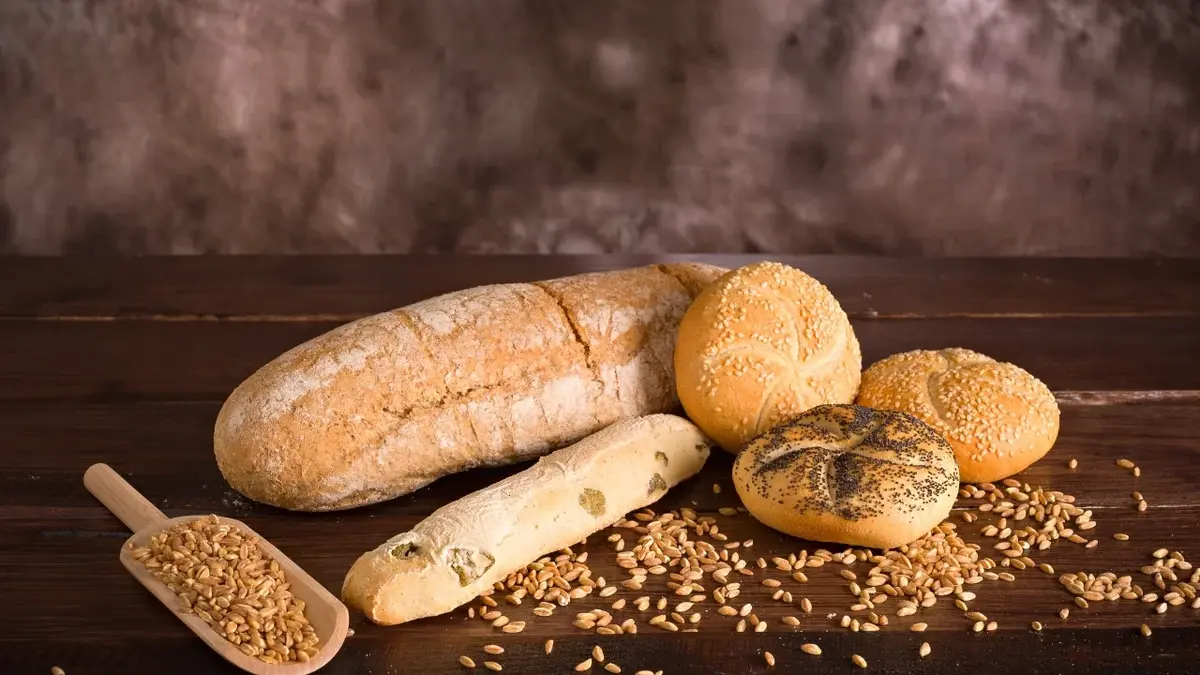 Chleb i bułki na drewnianym blacie, obok rozsypane ziarna zbóż 