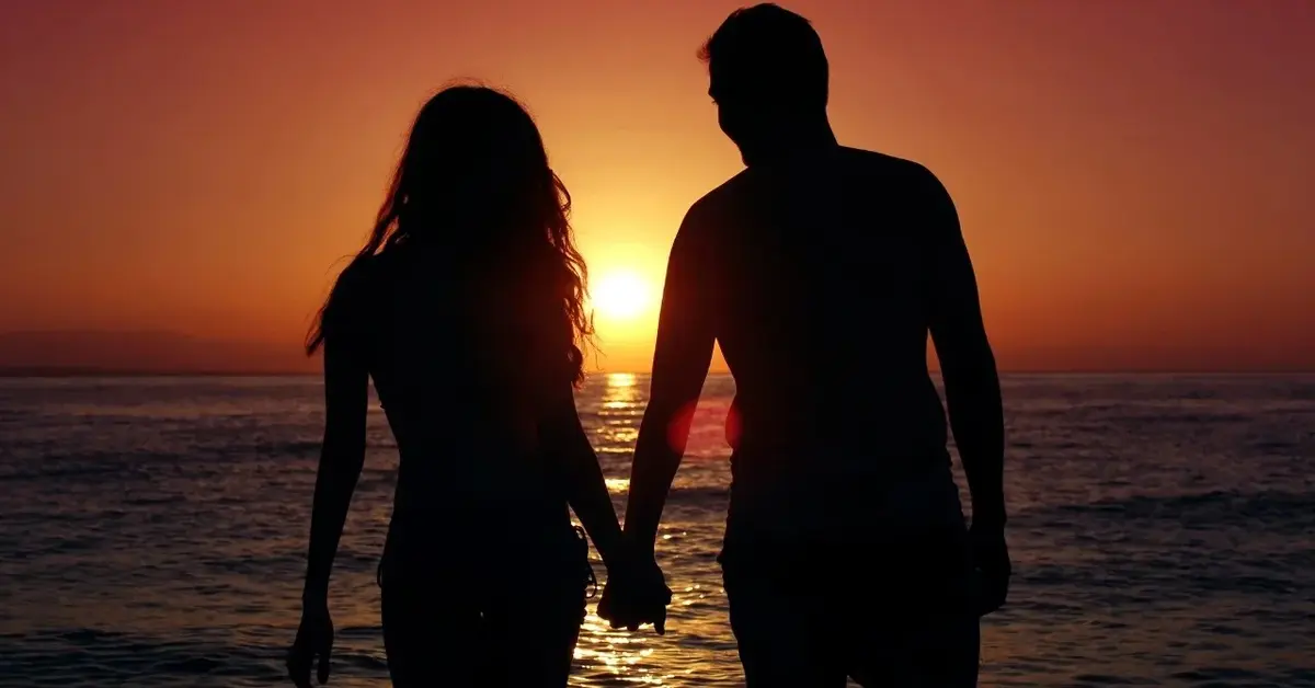 Para trzymająca się za ręce na tle zachodzącego słońca