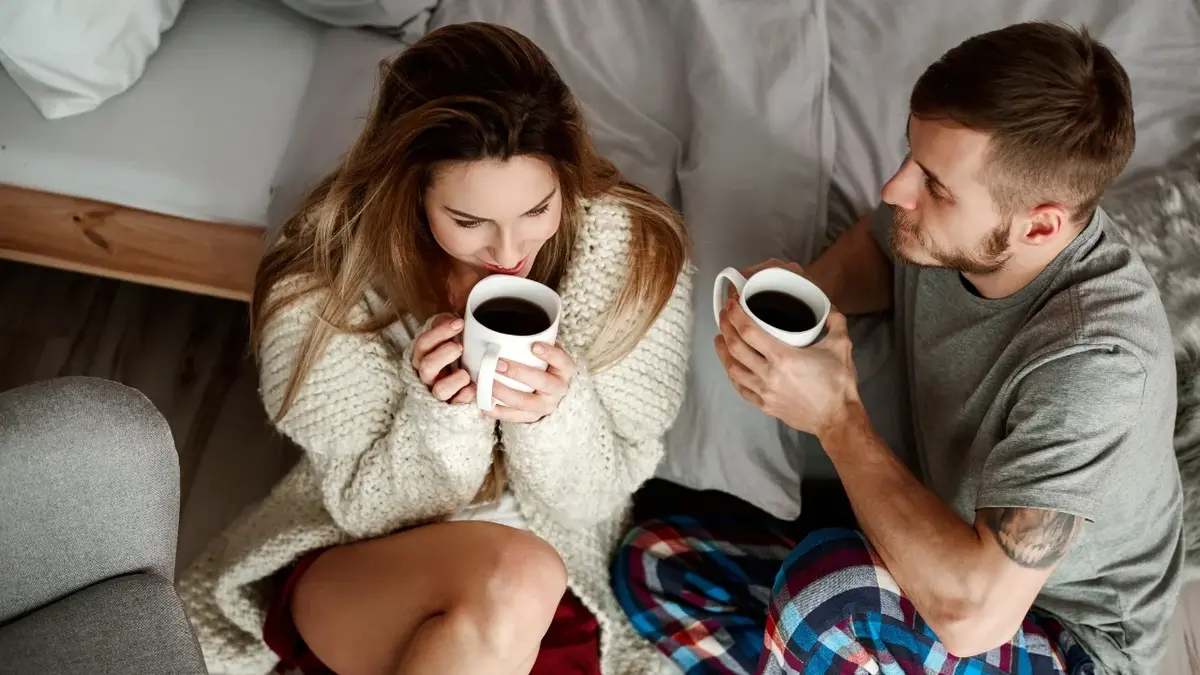 Kobieta i mężczyzna siedzący koło siebie z kubkami kawy w rękach 