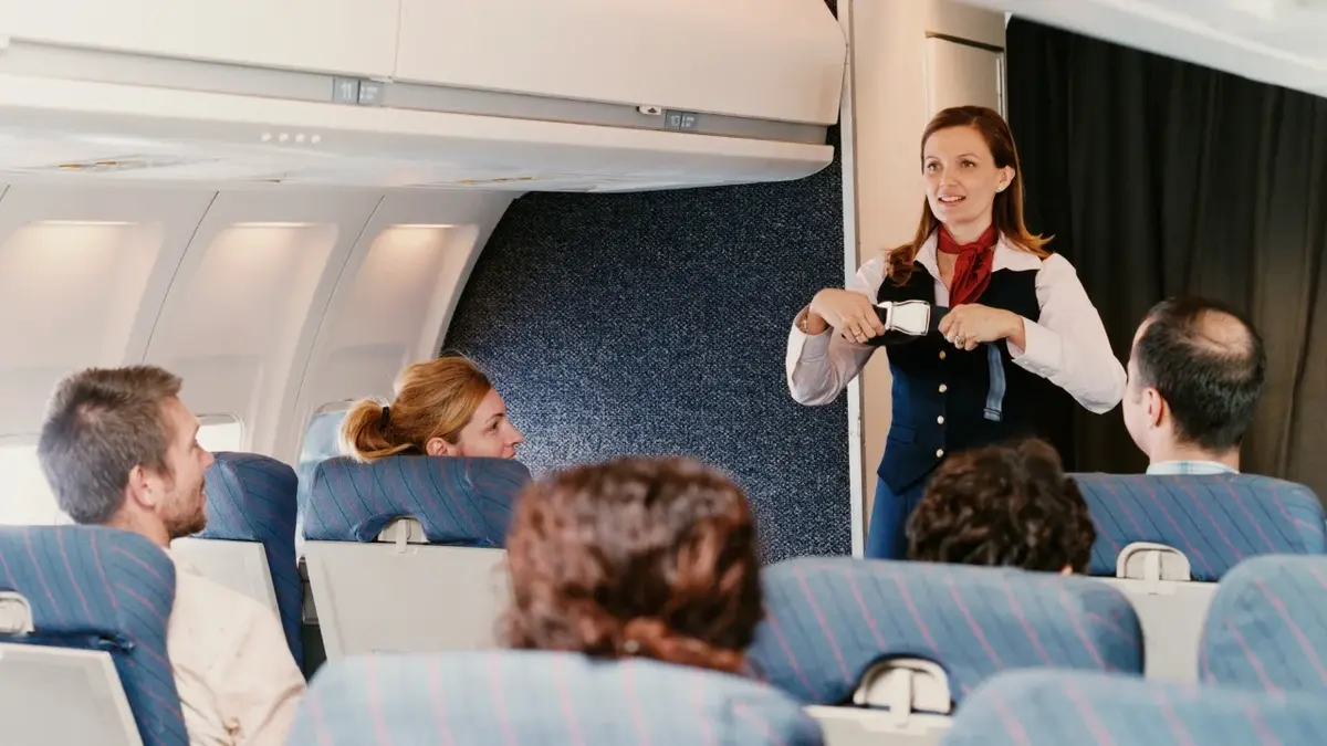 Stewardessa pokazująca na pokładzie samolotu instrukcje BHP