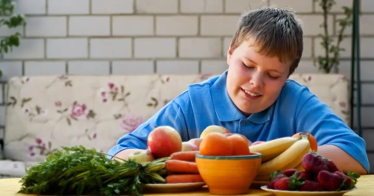 Chłopiec z nadwagą siedzący przy stole z warzywami 