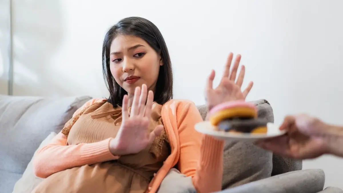 Kobieta siedząca na kanapie odmawiająca gestem dłoni podawanego burgera