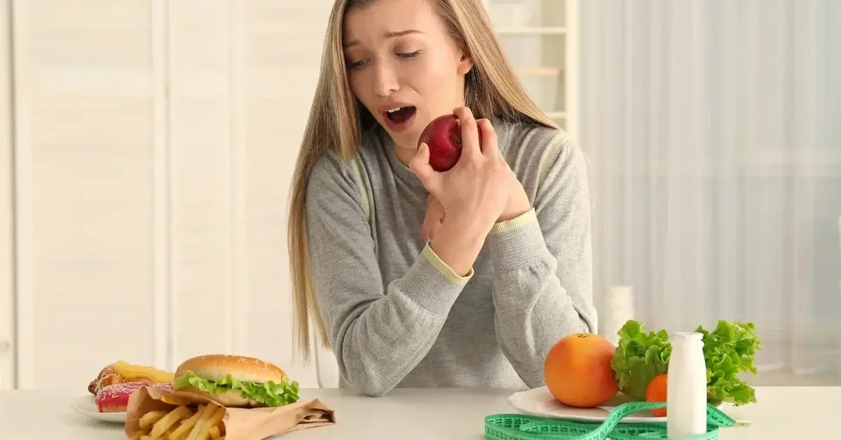Kobieta jedząca jabłko patrząca na tace z fast foodem