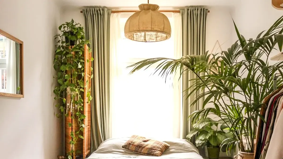 Zielone zasłony w białej, pełnej roślin sypialni
