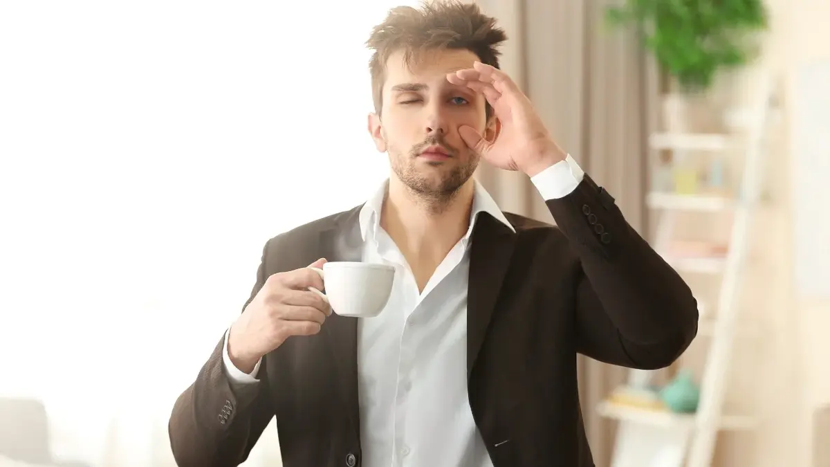 Zaspany mężczyzna z filiżanką kawy w ręku, próbuje się rozbudzić.